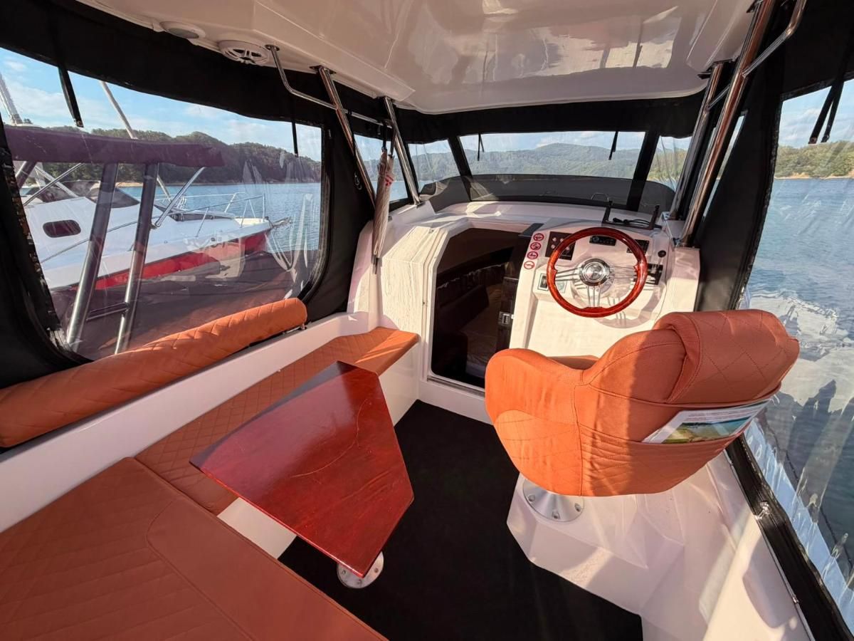 Wnętrze sterówki z pomarańczową tapicerką i widokiem na jezioro